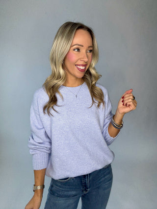 Woman wearing a sky blue sweater and blue jeans against a gray background