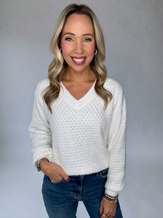 Woman wearing a white sweater and blue jeans against a gray background