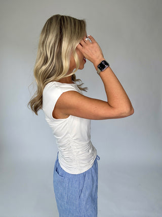 Woman wearing a white sleeveless top and blue pants against a plain background