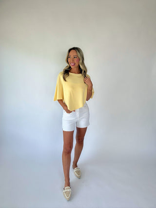 Woman wearing a yellow top and white shorts against a plain background