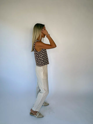 Woman wearing a patterned top and light-colored pants against a plain background