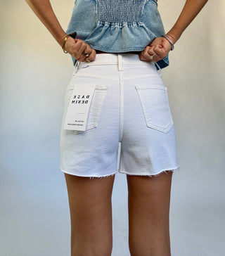 Person wearing white denim shorts with brand label on a plain background