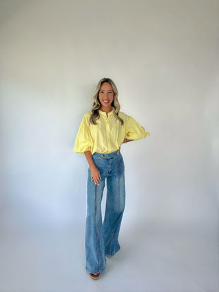 Woman wearing a yellow blouse and blue jeans against a plain background