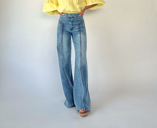 Person wearing a yellow blouse and blue jeans on a plain background