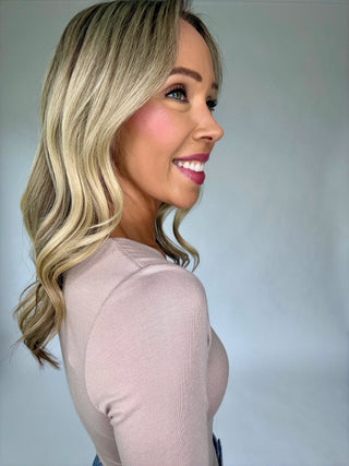 Woman with blonde hair and beige top against a plain background
