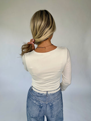 Person wearing a white long-sleeve top and blue jeans with a plain background