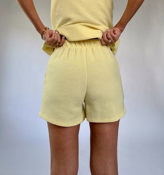Person wearing a yellow textured outfit with shorts on a plain background