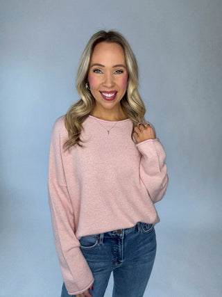 Woman wearing a pink sweater and blue jeans against a gray background