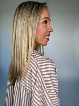 Woman with long blonde hair wearing a striped shirt against a plain background
