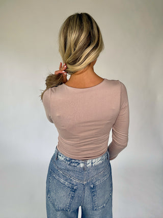 Person wearing a beige long-sleeve top and blue jeans against a plain background