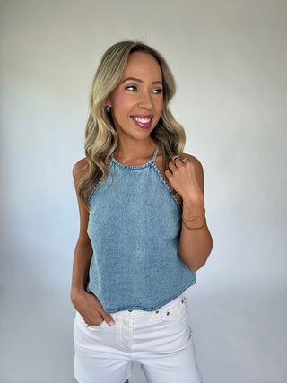 Woman wearing a blue sleeveless top and white pants against a plain background