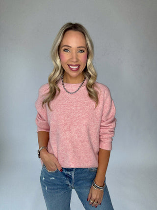 Woman wearing a pink sweater and blue jeans against a gray background
