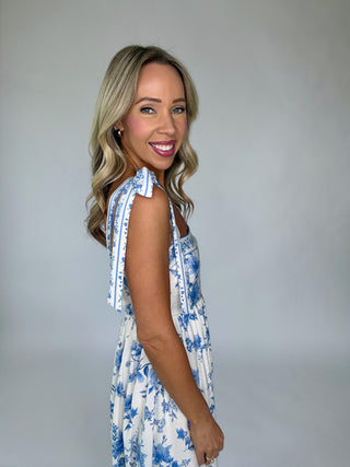 Woman wearing a blue and white floral dress against a plain background