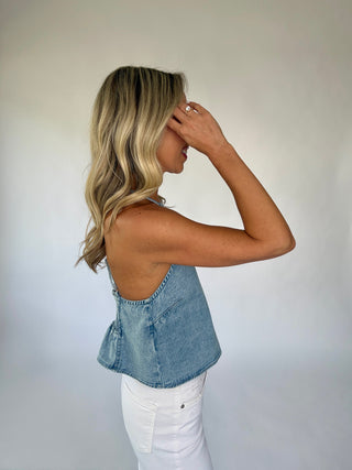 Woman wearing a denim top and white pants against a plain background