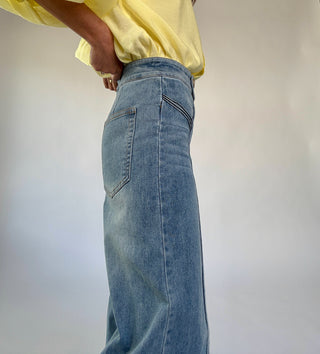 Person wearing blue jeans and a yellow top against a plain background