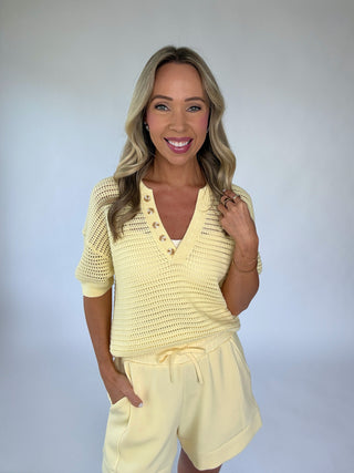 Woman wearing a yellow crochet top and shorts set against a plain background