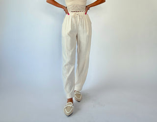 Person wearing a beige outfit with high-waisted pants on a light gray background