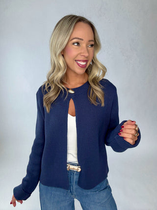 Woman wearing a navy blue jacket over a white top and blue jeans on a plain background