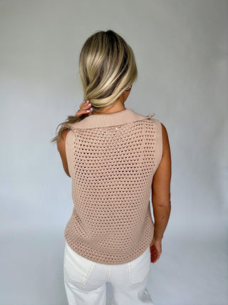Woman wearing a beige crochet sleeveless top against a plain background
