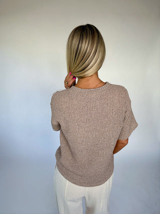 Person wearing a beige knitted sweater against a plain background