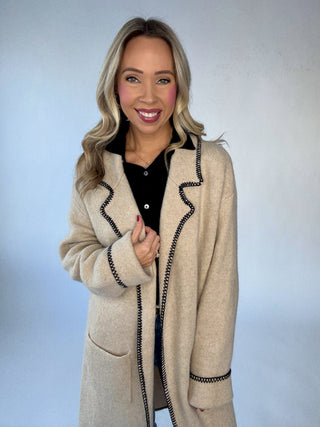 Woman wearing a oatmeal colored cardigan with black whipstitch detail