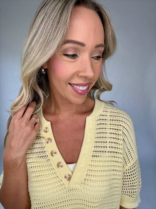 Woman wearing a light yellow knit cardigan with pearl buttons against a gray background