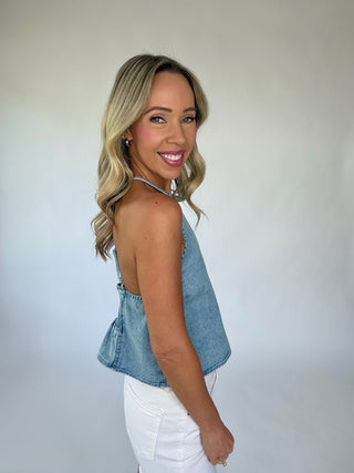 Woman wearing a denim top and white pants against a plain background