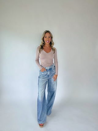 Woman wearing a beige long-sleeve top and blue jeans against a plain background