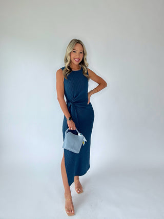 Woman wearing a blue dress holding a matching handbag against a white background