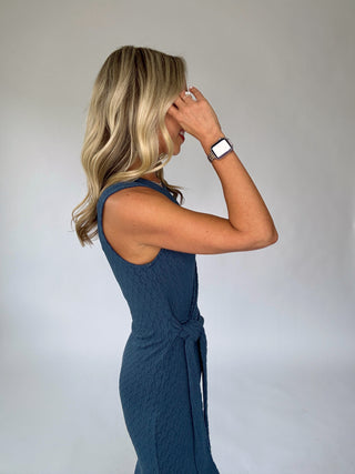 Woman wearing a blue sleeveless dress against a plain background