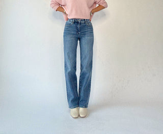 Person wearing a pink sweater and blue jeans against a plain background