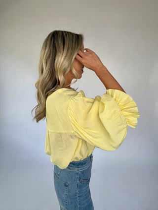 Woman wearing a yellow blouse with puffed sleeves against a plain background