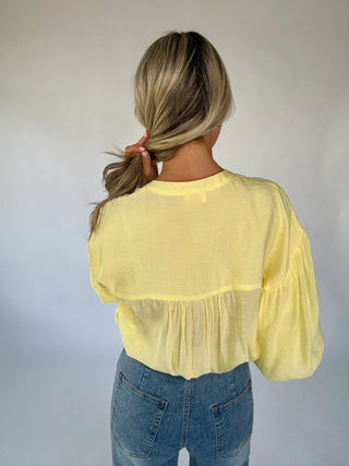 Person wearing a yellow blouse with puffed sleeves and blue jeans against a plain background