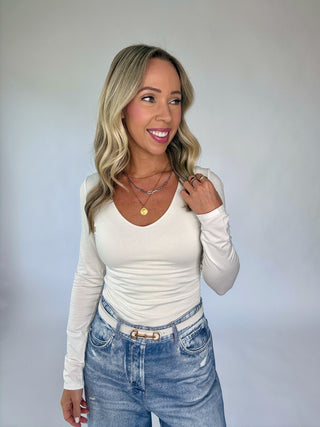 Woman wearing a white long-sleeve top and blue jeans against a plain background