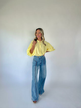 Woman wearing a yellow blouse and blue jeans against a white background
