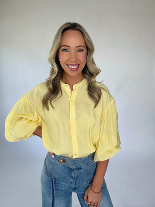 Woman wearing a yellow blouse and blue jeans against a plain background