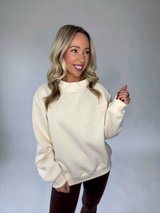 Women wearing a plush cream mock neck sweatshirt with brown legging against a gray background