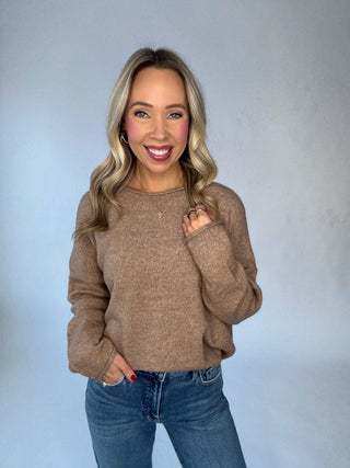 Woman wearing a brown sweater and blue jeans against a plain background