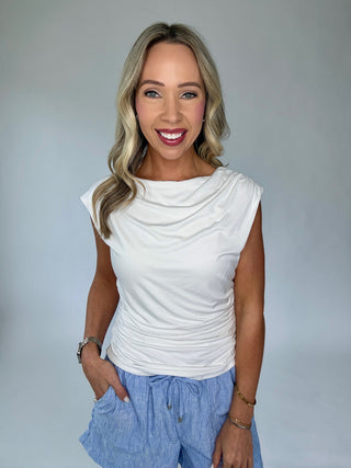 Woman wearing a white sleeveless top and blue pants against a plain background