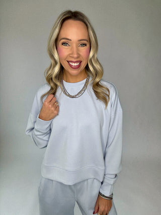 Woman wearing a light halogen blue sweatshirt and pants against a plain background