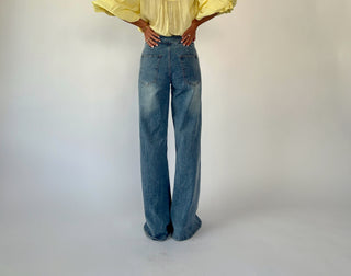 Person wearing a yellow blouse and blue jeans on a plain background