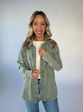 Woman wearing a green denim jacket over a white shirt with a plain background