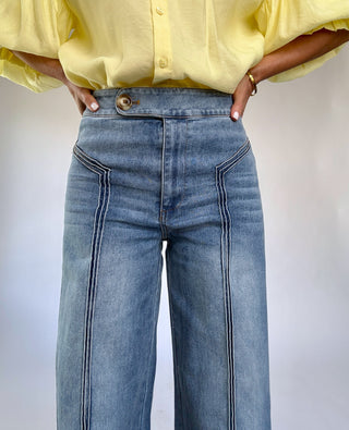 Person wearing a yellow blouse and blue jeans against a plain background