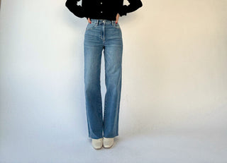 Person wearing blue jeans and a black top against a white background