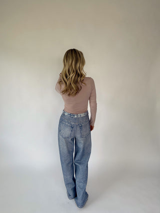 Person wearing a beige top and blue jeans against a plain background