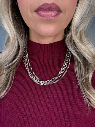 Close-up of a person wearing a maroon sweater and silver chain necklace with a blurred background