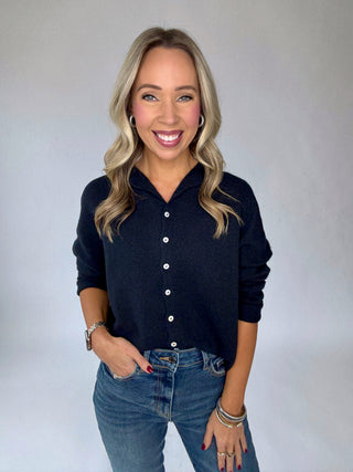 Woman wearing a navy button-up shirt and blue jeans against a plain background