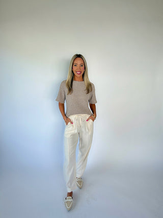 Woman wearing a gray sweater and white pants against a plain background