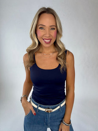 Woman wearing a navy tank top and blue jeans against a plain background