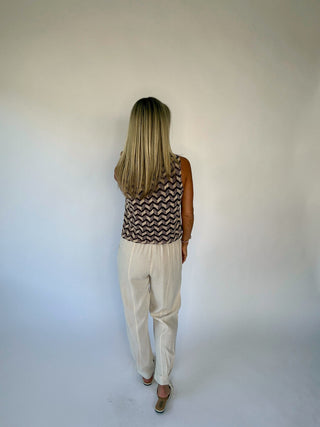 Person wearing a patterned top and beige pants against a white background